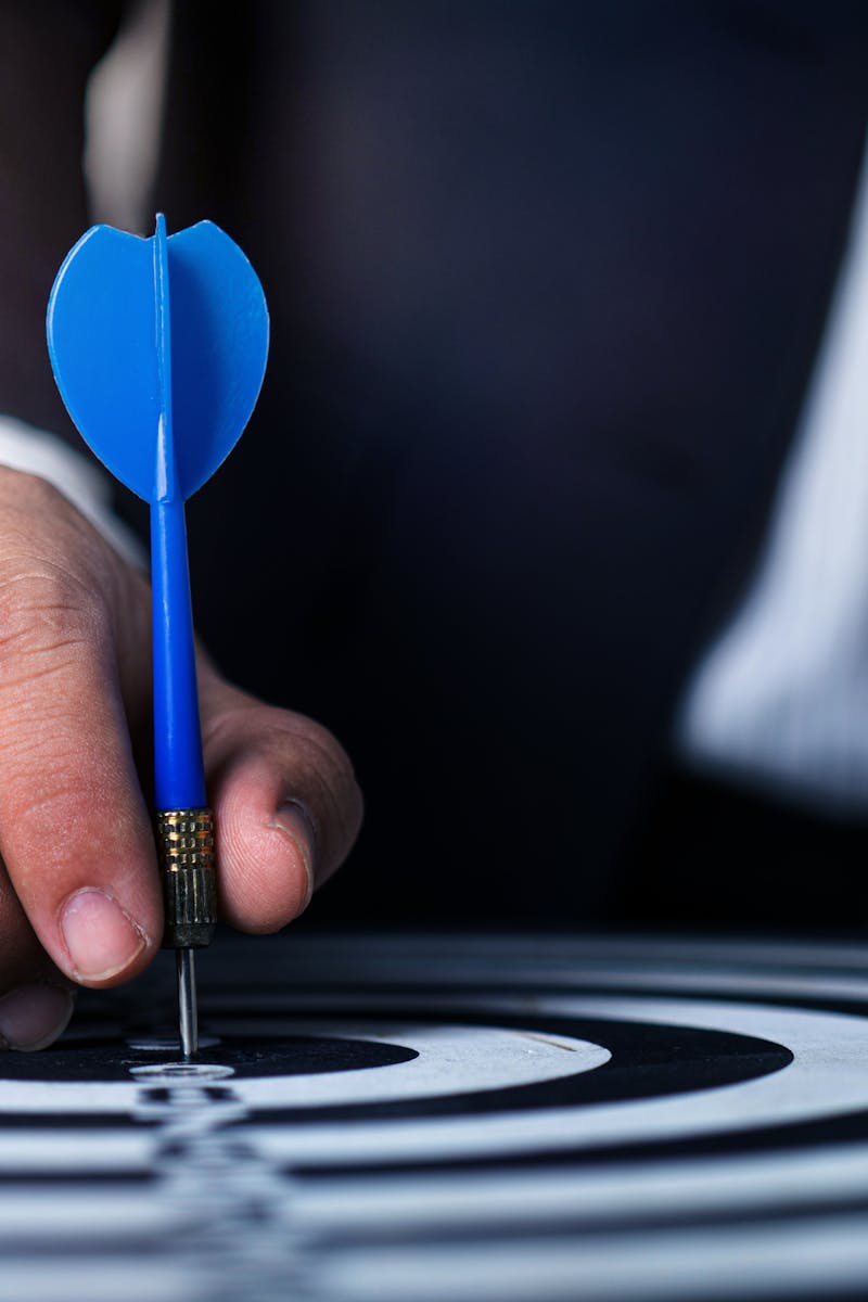 Close-up of a man's hand holding a blue dart on a bullseye, symbolizing precision and focus.